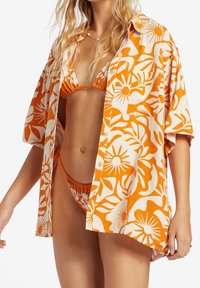 Koszulka w pomarańczowo-kremowy wzór o luźnym kroju, zapinana na guziki, z krótkimi rękawami, nałożona na pomarańczowy zestaw bikini.
