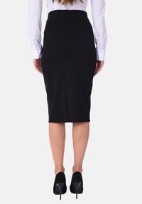 Gonna nera attillata con una trama liscia e lunghezza a metà polpaccio, dotata di uno spacco posteriore per facilitare il movimento. Indossata con scarpe con tacco alto nere.
