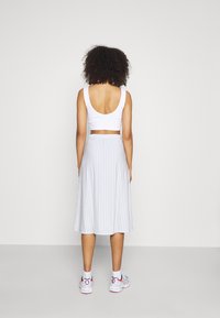 White sleeveless crop top with a low back; light blue and white striped knee-length skirt; worn with colorful athletic shoes.