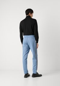Blå mønstrede bukser med elastisk liv, sidestriper, kombinert med en svart langermet topp og svarte sko.