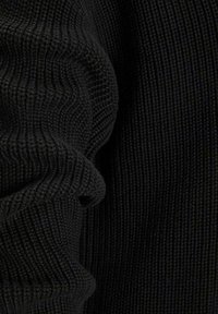 Gros plan sur un tissu en maille côtelée noir avec une texture et des plis visibles, mettant en valeur un matériau doux et épais.