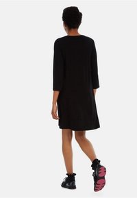 Svart knälång klänning med trekvartsärmar. Bärs med svarta sneakers med rosa sulor. Slätt tyg och enkel design.