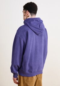 Sudadera con capucha morada de corte relajado, textura suave y puños acanalados. Presenta una parte trasera espaciosa con un diseño sencillo.