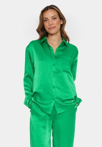 Green satin button-up shirt with a chest pocket, long sleeves, and loose design, paired with matching pajama-style pants.
