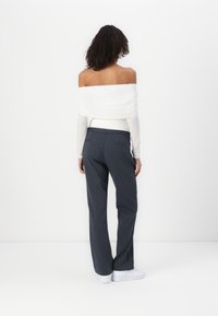 Off-the-shoulder white top paired with dark gray pinstriped trousers and white sneakers. The fabric appears smooth with a fitted silhouette.