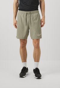 Pantaloni corti verdi da uomo con cintura elastica, stringa, tasche laterali e un logo Nike marrone chiaro stampato sulla gamba destra in basso.