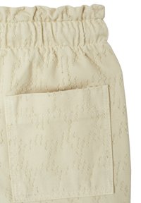 Light beige pants with a textured fabric, featuring a gathered elastic waistband and a functional side pocket.