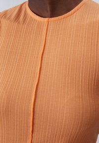 Persikofärgad veckad topp med rund halsringning. Texturerad tyg med vertikala linjer och en mittsöm som accent. Slät finish.