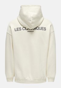 Hoodie en coton de couleur crème, doté d'une capuche, de poignets côtelés et d'un texte au dos indiquant « LES CLASSIQUES » et « ORIGINAUX » en gris foncé.