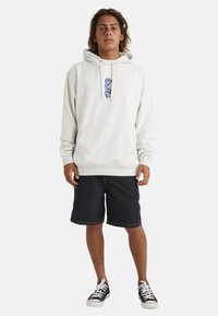 Light gray hoodie with front pocket, drawstrings, and purple graphic design. Paired with black shorts and white sneakers.