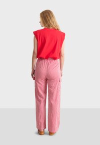 Top rosso senza maniche abbinato a pantaloni a vita alta e gamba larga con un motivo a righe verticali rosse e bianche. Fit casual e rilassato.