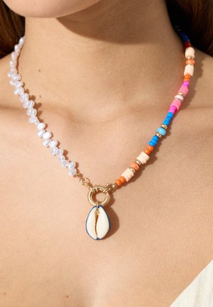 Zbliżenie na naszyjnik z koralików z białymi perłami, kolorowymi koralikami i białym zawieszonym muszlą na szyi i obojczyku osoby.