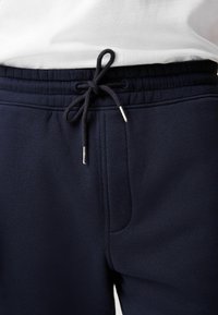 Pantalones deportivos azul marino con una cintura ajustable mediante cordón, que cuentan con elegantes bolsillos laterales y una suave textura de tela. Cordón ajustable con puntas metálicas.