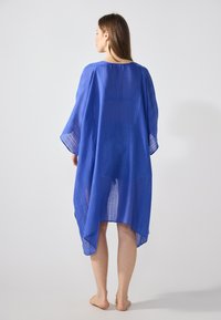 Blå, lätt kaftan med en avslappnad passform, som har breda ärmar och en hög-låg fåll. Texturerat tyg med subtila randiga mönster.