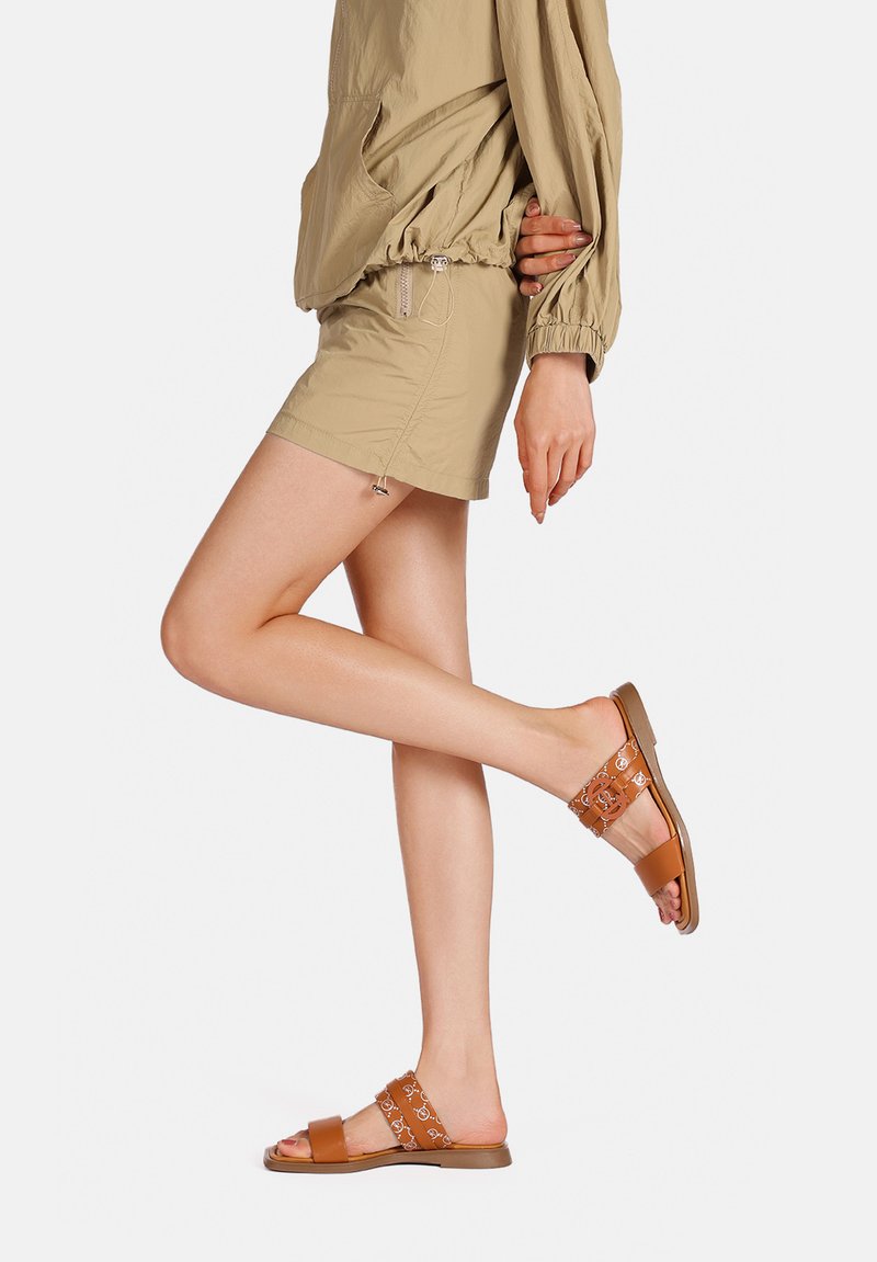 Sandali slide color tan con due cinghie, una liscia marrone e l'altra decorata in marrone chiaro e crema, abbinati a pantaloni corti khaki.