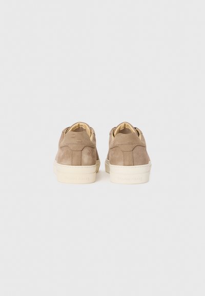 Beige nubukist sneakerid kreemikaalsete talladega, vaadatuna tagant, helevalge tausta ees.