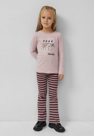 Hellrosa Langarmhemd mit grafischen Tänzern und dem Text "Du kannst mich Prinzessin nennen". Gestreifte kastanienbraune und rosa Schlaghosen. Schwarze Schuhe.