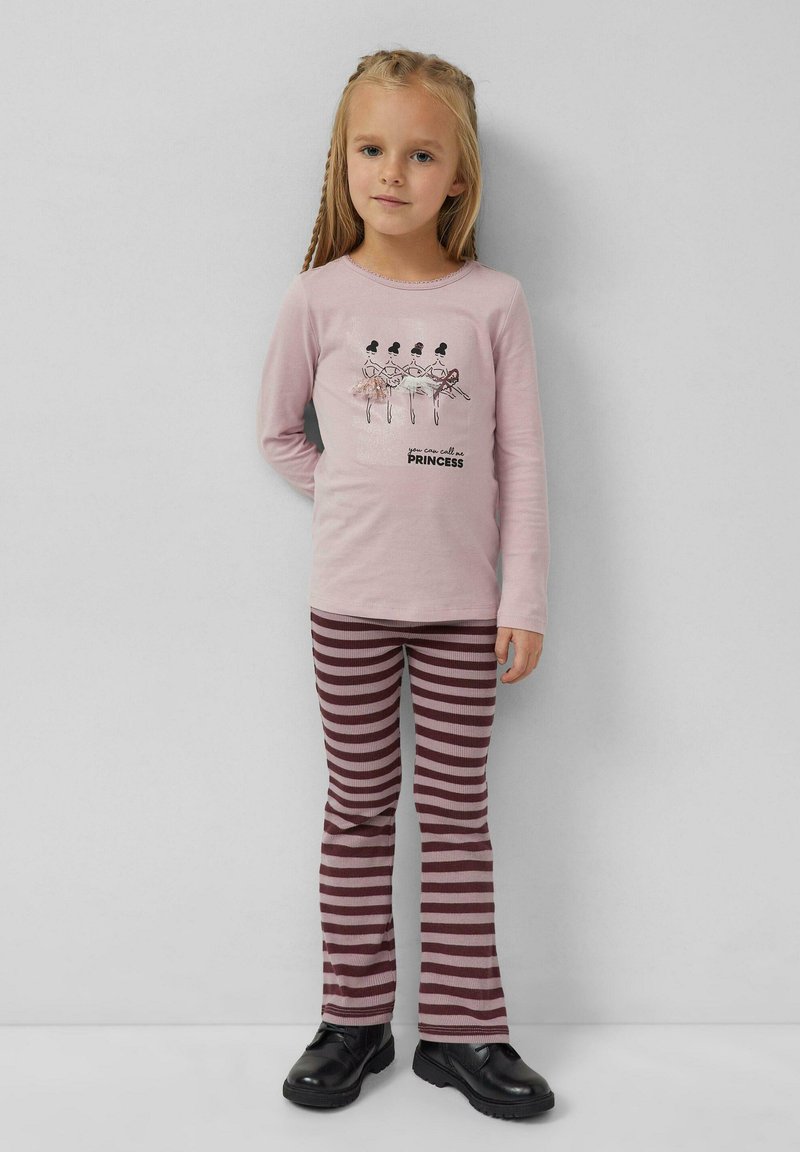 Hellrosa Langarmhemd mit grafischen Tänzern und dem Text "Du kannst mich Prinzessin nennen". Gestreifte kastanienbraune und rosa Schlaghosen. Schwarze Schuhe.