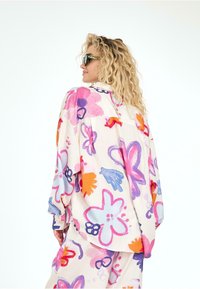 Chemise à motif floral, décontractée et en tissu léger. Présente des couleurs vives telles que le rose, le violet et l'orange, avec un col et des détails de bouton.
