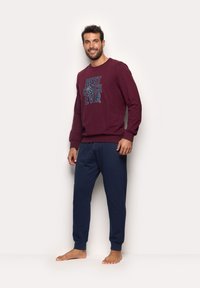 Maroon sweatshirt with “BEST COACH EVER” graphic in blue, paired with navy sweatpants. Soft cotton blend, relaxed fit, ribbed cuffs. No shoes.