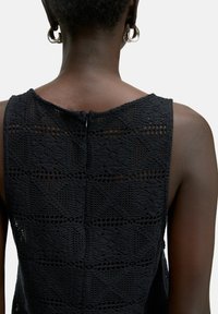 Zwarte mouwloze top met een getextureerd brei ontwerp met geometrische patronen en een rits aan de achterkant.