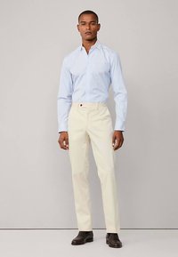 Vaaleansininen raidallinen kauluspaita, jossa valkoiset housut ja ruskeat nahkakengät. Klassinen kaulus ja räätälöity leikkaus. Sileä pinta.