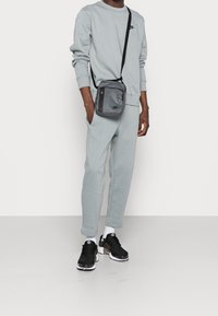 Ljusgrå sweatshirt och joggers i mjukt tyg, kombinerade med en liten svart axelremsväska. Svarta sneakers med vita sulor.