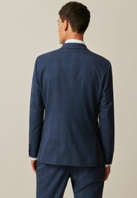 Chaqueta de traje a cuadros azul marino, hecha de una tela texturizada, con ajuste entallado, solapas escotadas y puños abotonados con detalles en plateado.