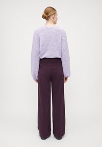 Lilla teksturert genser med brede ermer, kombinert med høyt liv og løstsittende mørkelilla bukser. Minimalistisk design, uten synlige mønstre.