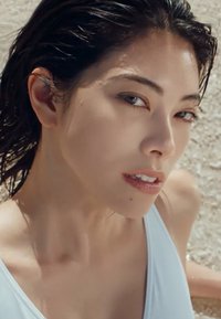 Gros plan sur une personne avec des cheveux sombres et mouillés, et une peau claire, portant un maillot de bain bleu clair, avec une texture lisse et peu de détails de design.