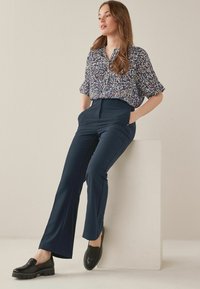 Mariene flared broek gecombineerd met een kortmouwige, gemêleerde blouse in blauw, wit en rood. Schoeisel: zwarte gevlochten instappers met een dikke zool.