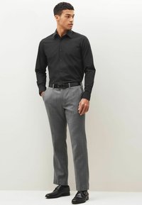 Camisa negra de manga larga combinada con pantalones texturizados gris claro. Un cinturón negro y zapatos completan el conjunto. Diseño limpio y ajustado.
