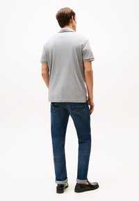 Polo gris avec un col simple, associé à un jean denim bleu foncé, coupe slim. Chaussures noires à finition brillante. Textures lisses.