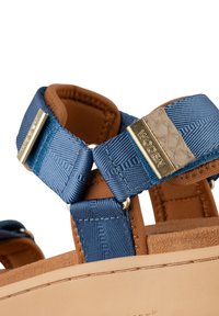 Blue and brown sandal with textile straps, gold hardware accents, and a textured tan sole. Features a padded interior for comfort.