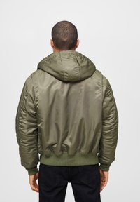 Olivgrön bomberjacka med huva, tillverkad av glansigt nylon, med elastiska ärmslut och nederkant, samt med sydda sidodetaljer.