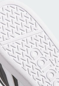Suela de zapatilla de goma blanca con un patrón en zigzag texturizado y logotipo en relieve, con acentos en negro en las secciones superiores.