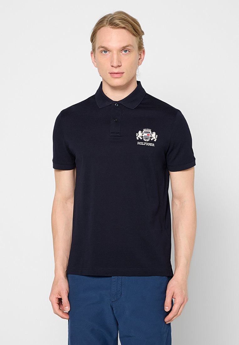Polo shirt bleu marine en coton, avec un col à deux boutons et un logo brodé sur le côté gauche de la poitrine. Manches courtes, coupe classique.