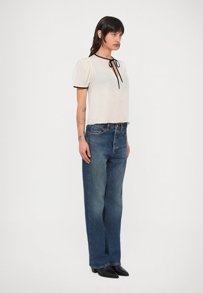 Vit, texturerad blus med puffärmar och svart kantband. Kombinerad med blå, högmidjade jeans med vida ben och svarta ankelboots.