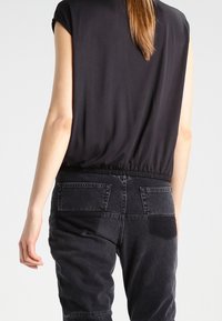 Haut noir à manches courtes avec taille cintrée, associé à un jean en denim noir taille haute avec poches arrière et un panneau texturé.