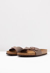 Rjave natikače na slip-on z zgornjim delom z teksturo, dvema širokima trakova in podrobnostjo z kovinsko sponko. Korken podplat z vzorčastim gumijastim zunanjim delom.