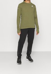 Grøn langærmet sports skjorte med en tekstureret overflade, parret med sorte sweatpants med grå sidelister og sorte træningssko.
