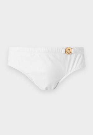 Hvid bikinitrusse med elastisk taljebånd og en lille guldfarvet smiley-vedhæng fastgjort til en hvid sidestrop.