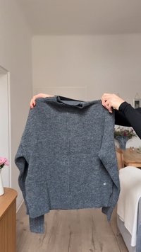 Siv pulover iz pletenine z zaobljenim izrezom, spuščena ramena in teksturirano zaključeno površino. Na strani ima manjši logotip.