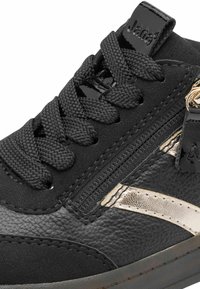 Black sneaker featuring a mix of textured synthetic materials, a side zipper, and a metallic gold accent. Thick black laces complete the design.