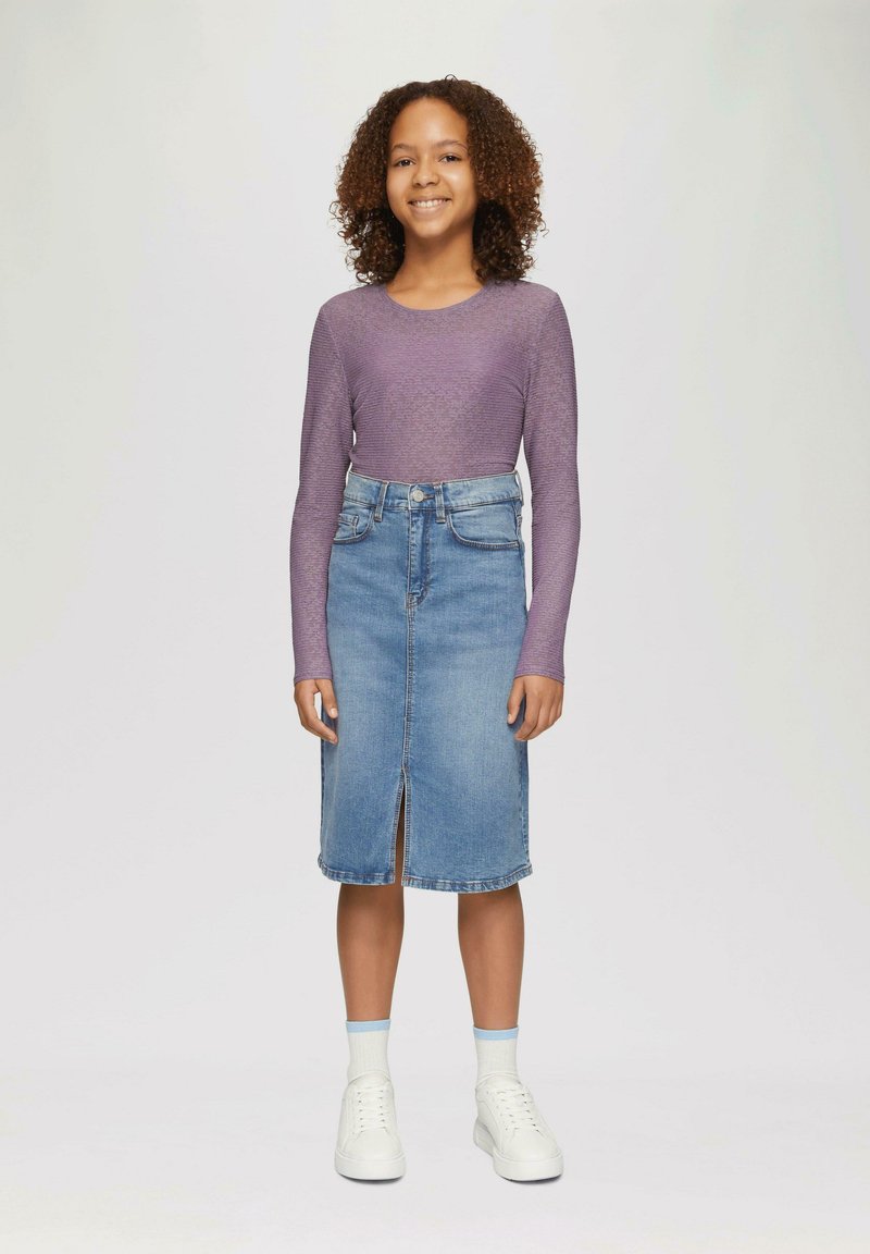 Langdurige paarse top met een geribbeld patroon, gecombineerd met een lichtblauwe denim kokerrok met een split aan de voorkant, en witte sneakers.
