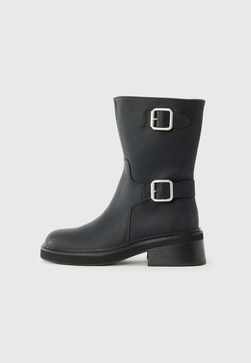 Botas de cuero negras hasta el tobillo con dos hebillas plateadas, puntera redondeada y tacón grueso. La textura es lisa con un ligero brillo.