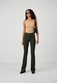 Μπεζ αμάνικο τοπ συνδυασμένο με ψηλόμεσο, σκουροπράσινο παντελόνι καμπάνα. Το μοντέλο φοράει μαύρα γυαλιά ηλίου και κρατάει μια μικρή μαύρη τσάντα.