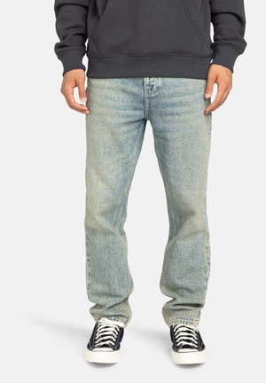 Person wearing light blue straight-fit jeans, black and white sneakers, and a dark gray sweatshirt with hands relaxed at sides.