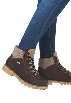 Brown leather hiking boots with felt cuff, lace-up design, rugged sole, and side zipper. Detailed stitching and gold branding accent.