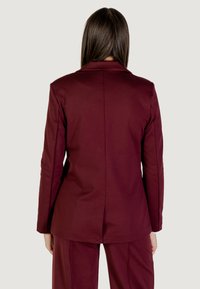 Burgundy blejzr vyrobený z hladkého materiálu, s vrškem se zářezem a přizpůsobeným střihem. Zadní pohled zvýrazňuje středový šev a strukturovanou siluetu.